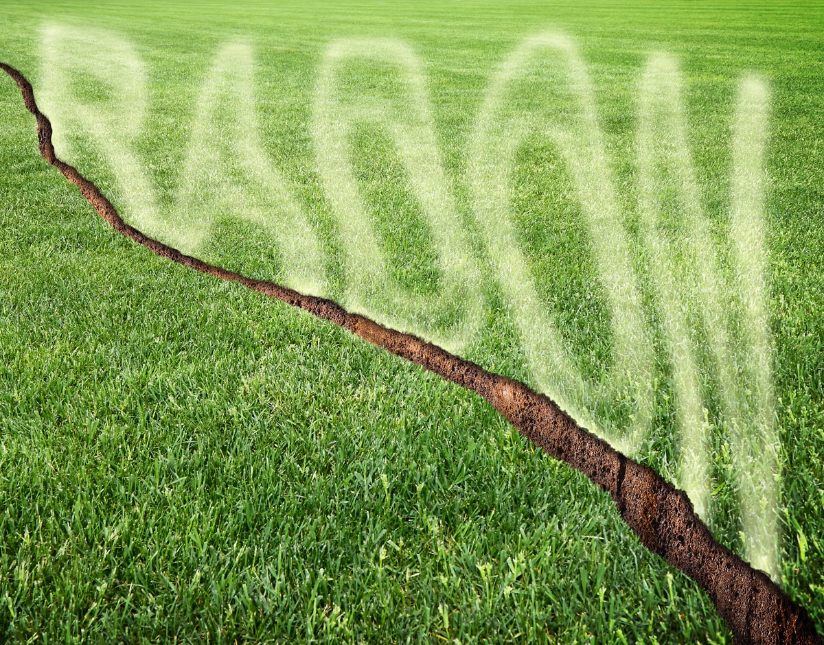 Une pelouse verte tondue présentant une fissure en diagonale d'où s'échappe du gaz radon.